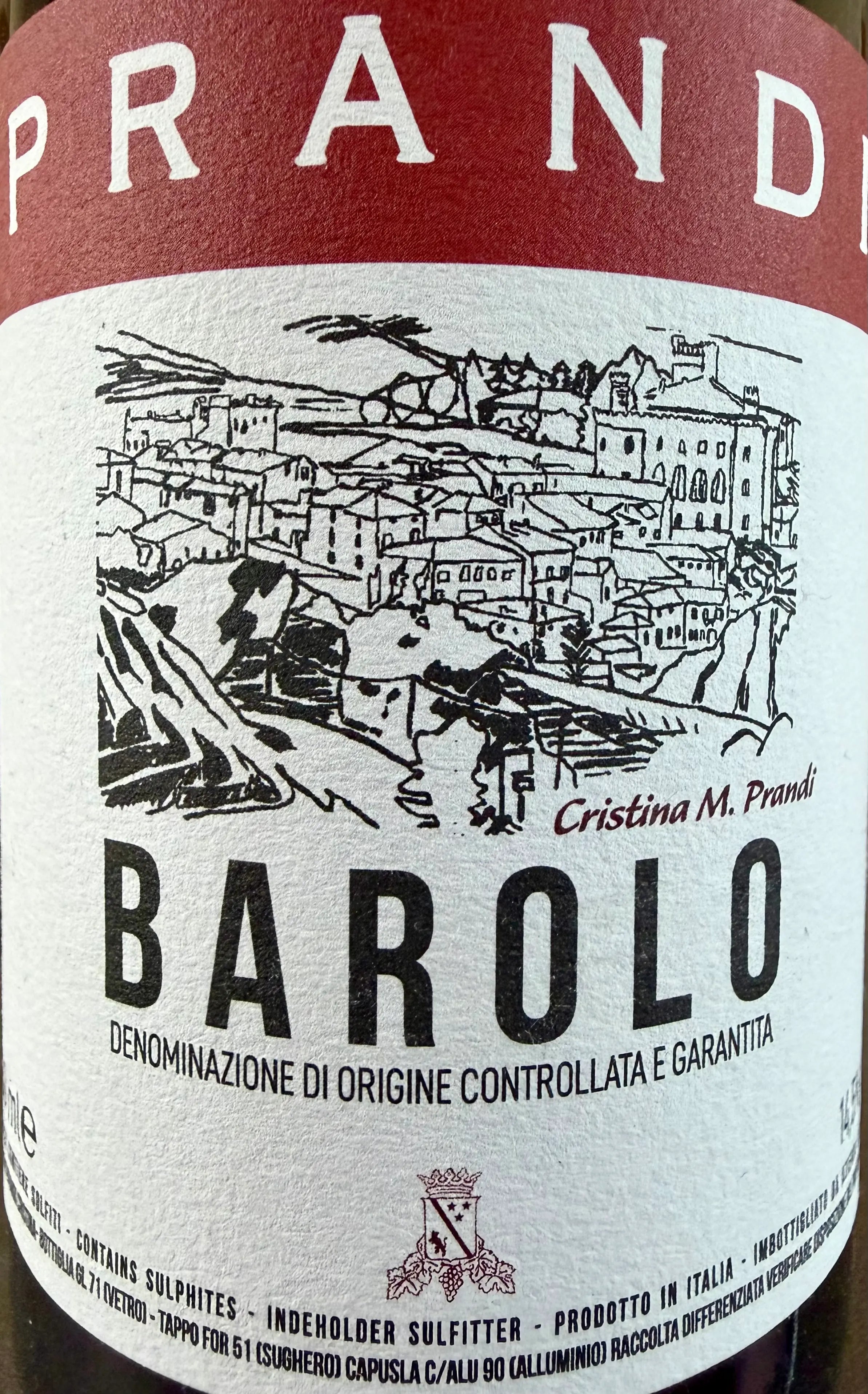 Close-up of a wine label reading PRANDI BAROLO, with a red top band, white label background, black illustrated town scene, and large BAROLO text.